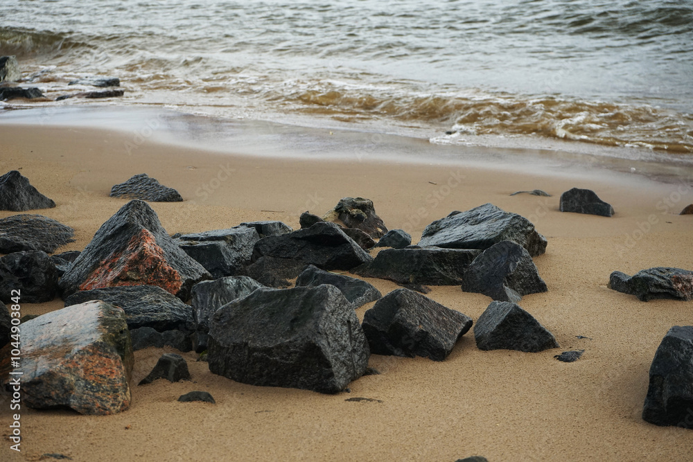 Obraz premium Sandy beach with large black stones in non-sunny weather