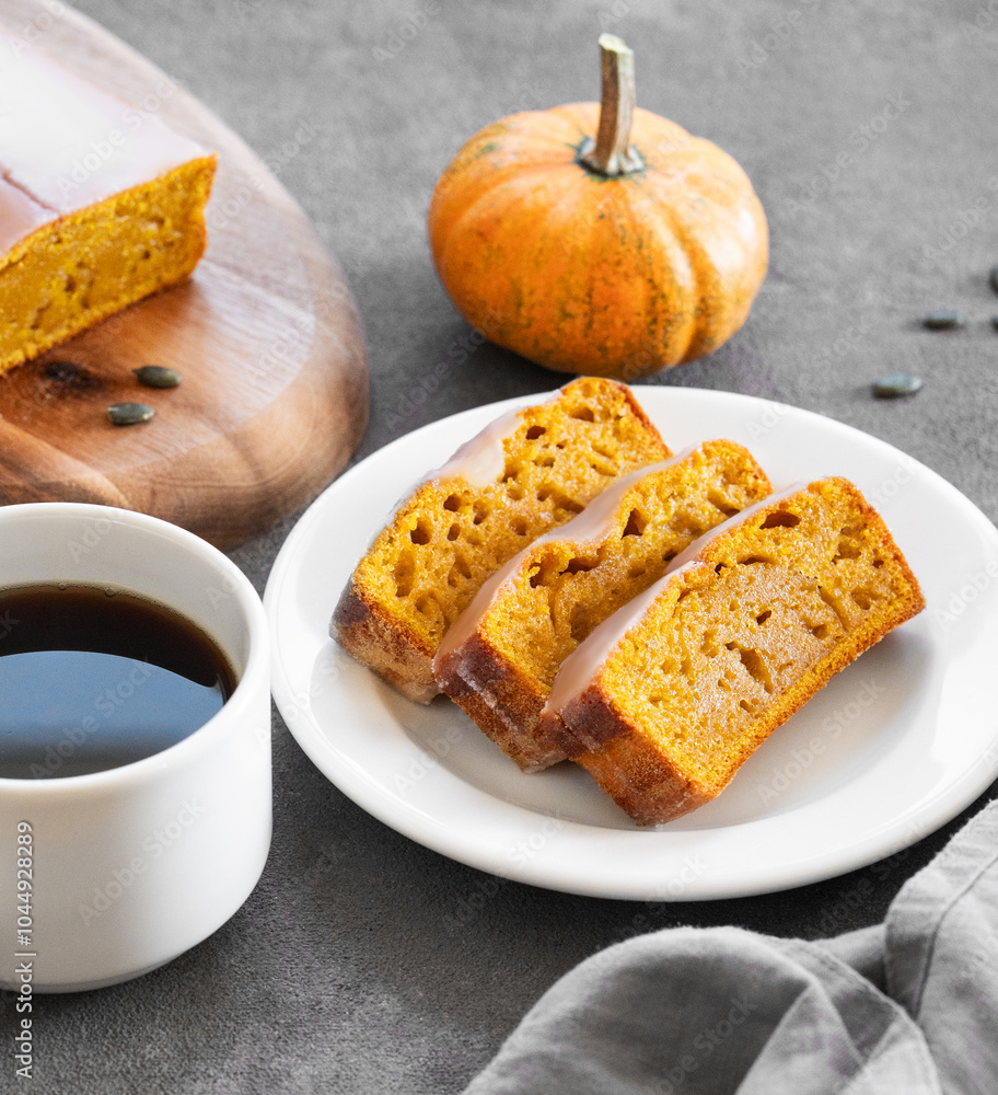 Pumpkin sweet bread or cake with icing on a plate on a dark background with decorative pumpkins and a cup of coffee. Pumpkin sweet bread or cake with icing on a plate on a dark background with decorative pumpkins and a cup of coffee.