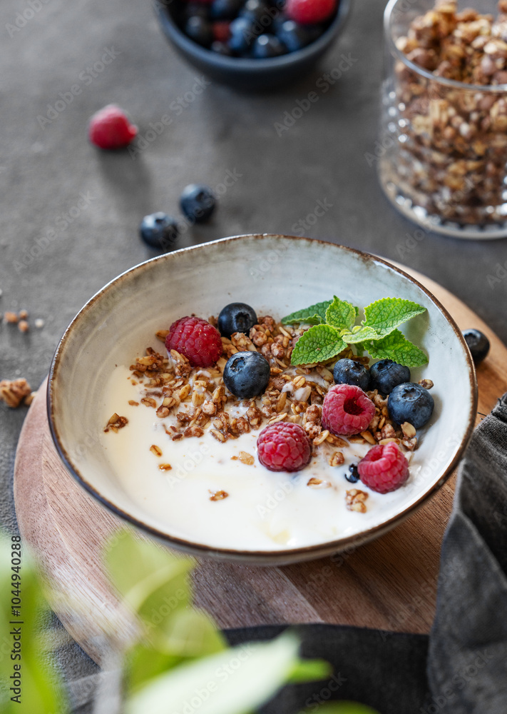 Granola with greek yogurt, raspberries and blueberries in a bowl on a dark background with fresh berries and leaves. Granola with greek yogurt, raspberries and blueberries in a bowl on a dark background with fresh berries and leaves.
