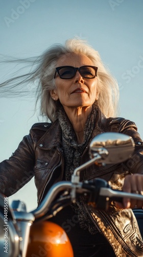 A woman with gray hair is sitting on a motorcycle wearing sunglasses