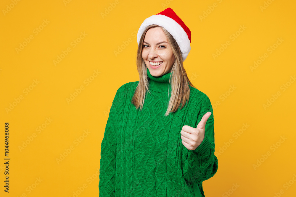 Merry smiling cool young woman wears green warm cozy sweater Santa hat posing showing thumb up like gesture isolated on plain yellow background. Happy New Year, celebration Christmas holiday concept. Merry smiling cool young woman wears green warm cozy sweater Santa hat posing showing thumb up like gesture isolated on plain yellow background. Happy New Year, celebration Christmas holiday concept.