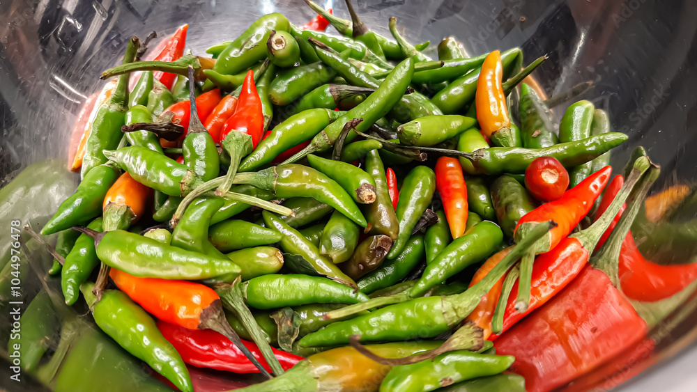 A Bunch of Small Green, Red, Orange Shiny Cayenne Peppers in a Stainless Steel Bowl Close Up. Raw Materials for Sambal Spices and Asian Spices, Especially Indonesia and India. Fresh Condition Fruits A Bunch of Small Green, Red, Orange Shiny Cayenne Peppers in a Stainless Steel Bowl Close Up. Raw Materials for Sambal Spices and Asian Spices, Especially Indonesia and India. Fresh Condition Fruits