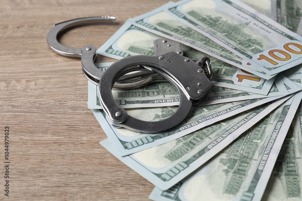 Corruption. Handcuffs and dollar banknotes on wooden table, closeup