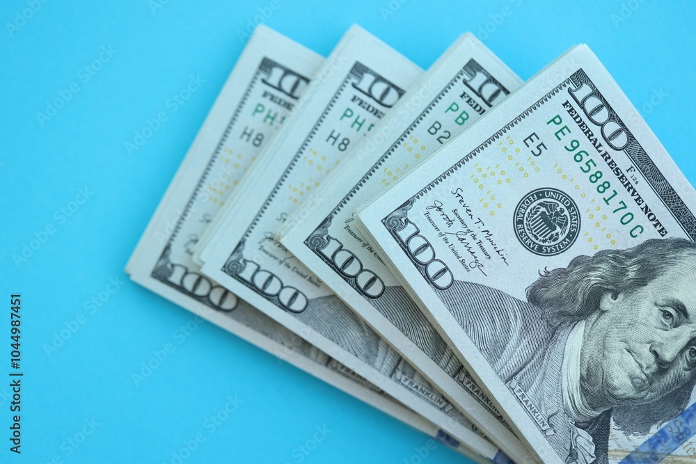 Big amount of hundred dollar bills in thick stack lies on bright blue color paper background Big amount of hundred dollar bills in thick stack lies on bright blue color paper background