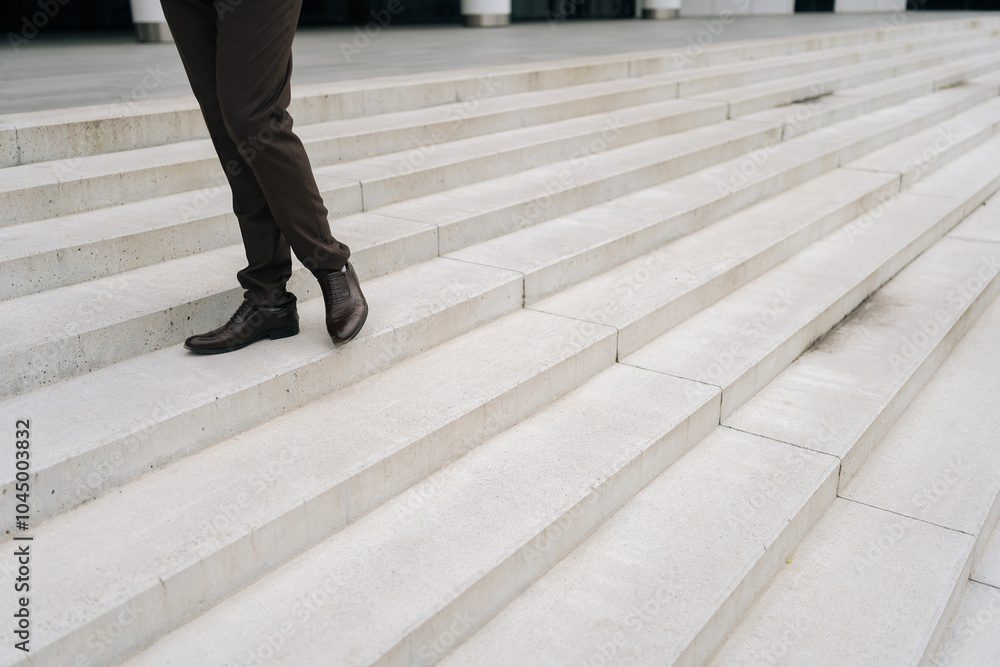 Cropped shot of unrecognizable businessman standing on steps outside contemporary corporate building. Closeup business man in formal shoes climbing stairs outside modern office building. Cropped shot of unrecognizable businessman standing on steps outside contemporary corporate building. Closeup business man in formal shoes climbing stairs outside modern office building.