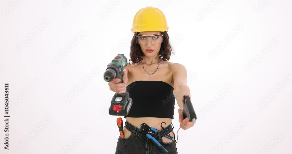 Woman construction worker crosses hands holding drills. Young female engineer in black top and safety glasses poses with mechanical tools slow motion Woman construction worker crosses hands holding drills. Young female engineer in black top and safety glasses poses with mechanical tools slow motion