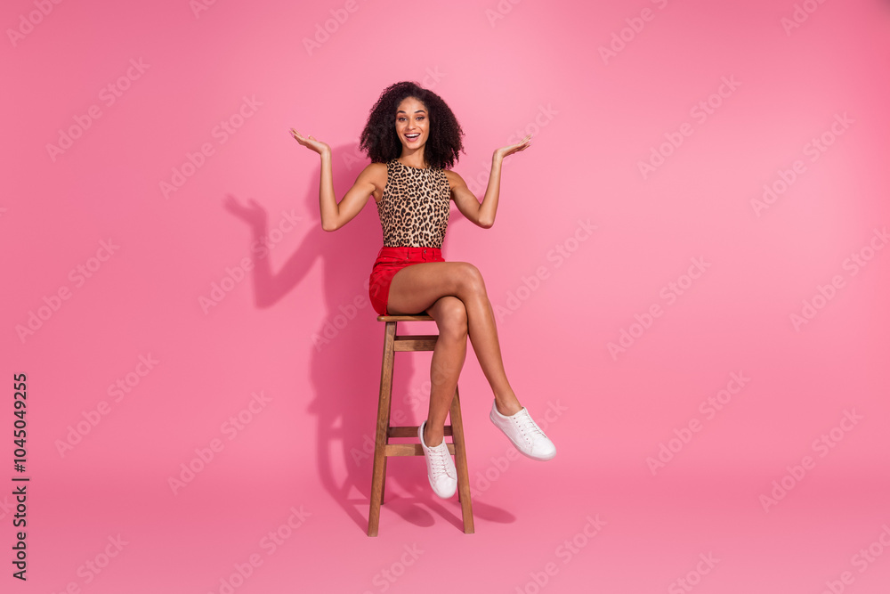 Full length photo of lovely young lady sit chair compare empty space wear stylish leopard print garment isolated on pink color background Full length photo of lovely young lady sit chair compare empty space wear stylish leopard print garment isolated on pink color background