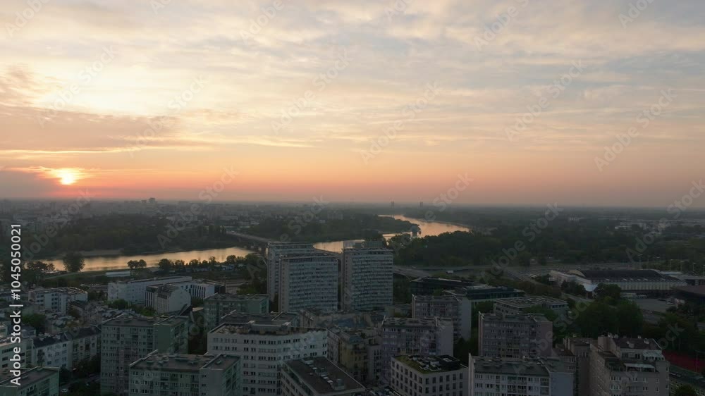 Aerial views showcase the sun setting over the Vistula River, casting light on Warsaw's vibrant cityscape and highlighting its stunning urban architecture at sunset Aerial views showcase the sun setting over the Vistula River, casting light on Warsaw's vibrant cityscape and highlighting its stunning urban architecture at sunset