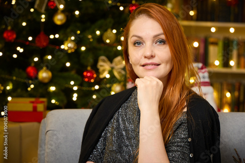 A beautiful woman is waiting for guests in the living room near the Christmas tree for a festive lunch.