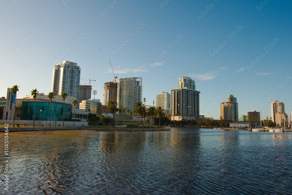 Obraz premium View from Albert Whitted Playground into south yacht basin in St. Petersburg, FL. Towards downtown skyline. Calm blue water with white puffy clouds. Marina and docked boats. Masts and sails against a 