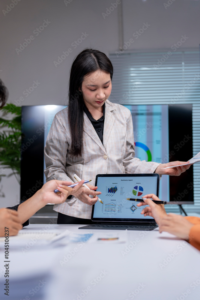 Asian businesswoman leading meeting pointing at tablet screen showing charts Asian businesswoman leading meeting pointing at tablet screen showing charts