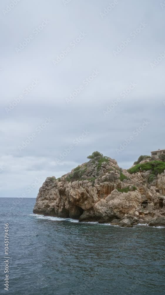 Rocky coastline of cala deia in mallorca, spain with an overcast sky and calm sea water Rocky coastline of cala deia in mallorca, spain with an overcast sky and calm sea water