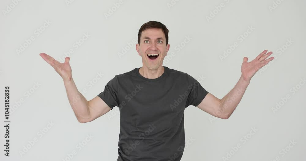 Man wearing dark grey t-shirt shrugs with surprised expression on white background. Emotional male shows shock of unexpected events development Man wearing dark grey t-shirt shrugs with surprised expression on white background. Emotional male shows shock of unexpected events development