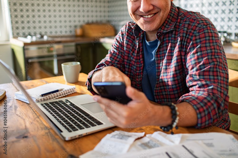 Close up man using smartphone with bills and laptop on kitchen desk Close up man using smartphone with bills and laptop on kitchen desk