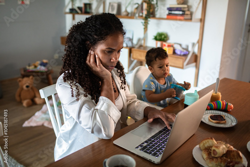 Busy mom working with laptop at home with toddler photo