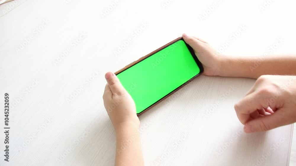 child's hands holding smartphone with horizontal green chromatic screen isolated on white. Mobile phone in hand. Various signs and gestures with fingers. Concept of technology and Internet. child's hands holding smartphone with horizontal green chromatic screen isolated on white. Mobile phone in hand. Various signs and gestures with fingers. Concept of technology and Internet.