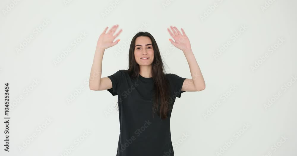 Cheerful young woman waves hands greeting friends on white background. Smiling brunette female in casual attire reflects positive attitude Cheerful young woman waves hands greeting friends on white background. Smiling brunette female in casual attire reflects positive attitude