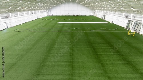 A time-lapse video showing the step-by-step construction of an indoor football field. The process includes rolling out the green turf, watering the grass, and marking the white lines.