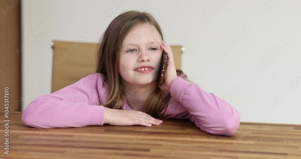 Cheerful schoolgirl talks on smartphone sitting at desk. Cute little girl with loose hair engages in positive conversation enjoying pleasant communication Cheerful schoolgirl talks on smartphone sitting at desk. Cute little girl with loose hair engages in positive conversation enjoying pleasant communication