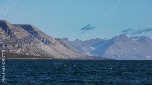 Vast blue waters embracing the rugged mountains of Svalbard during a clear sunny day