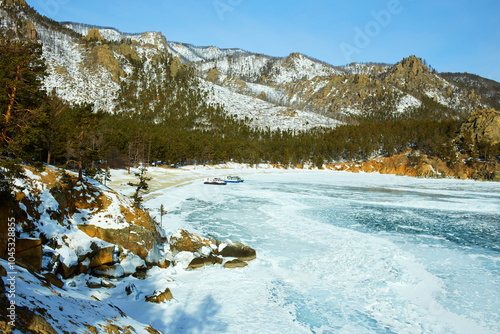 Lake Baikal in winter. A beautiful view of a frozen lake, a bay surrounded by mountains and forest, a hovercraft with tourists in the distance. Winter trip.  photo