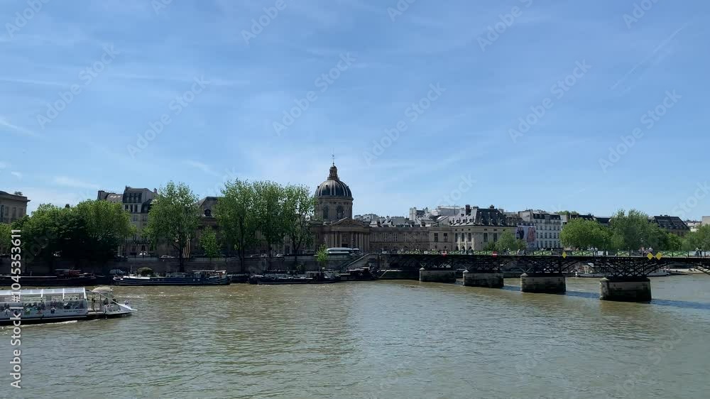 Seine River Cruise ship, boat full of tourists sails under Pont des Arts bridge. Institut de France and Parisian style buildings in the background. Movement of cars traffic and people. Paris, France Seine River Cruise ship, boat full of tourists sails under Pont des Arts bridge. Institut de France and Parisian style buildings in the background. Movement of cars traffic and people. Paris, France