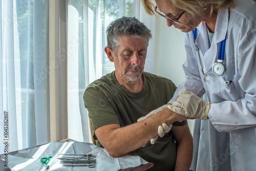 Mole check exam. A patient at 
 a DR's appointment. A female GP in a white coat checks her patient's skin for signs of cancer, whilst discussing treatment she takes a biopsy at the hospital clinic.