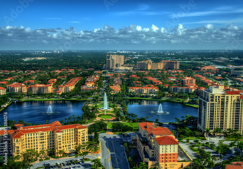 Neighbourhood Real Estate - Aerial view of a suburban area with lakes, fountains, and buildings under a blue sky.