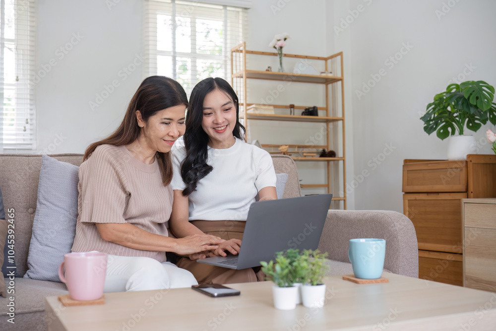 Elderly Mother and Daughter Enjoy Quality Time Together at Home, Smiling and Using a Laptop in a Cozy Living Room Setting Elderly Mother and Daughter Enjoy Quality Time Together at Home, Smiling and Using a Laptop in a Cozy Living Room Setting