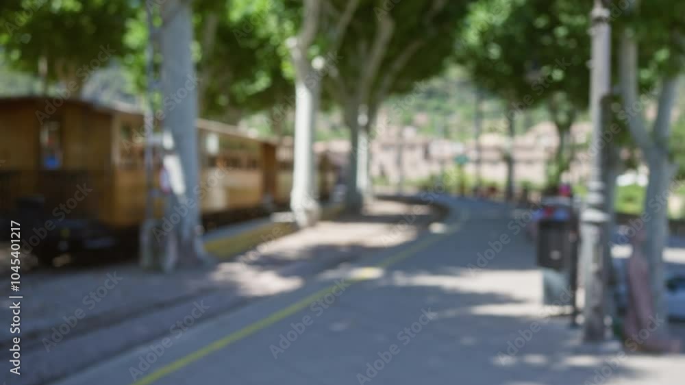 Blurry outdoor scene of a train station in mallorca with green trees lining the pathway and defocused wooden train in the background Blurry outdoor scene of a train station in mallorca with green trees lining the pathway and defocused wooden train in the background