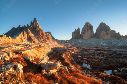 Majestic peaks of the Tre Cime di Lavaredo, Dolomites bathed in golden sunlight at dusk as the rugged landscape showcases nature’s beauty in Italy's renowned mountain range.