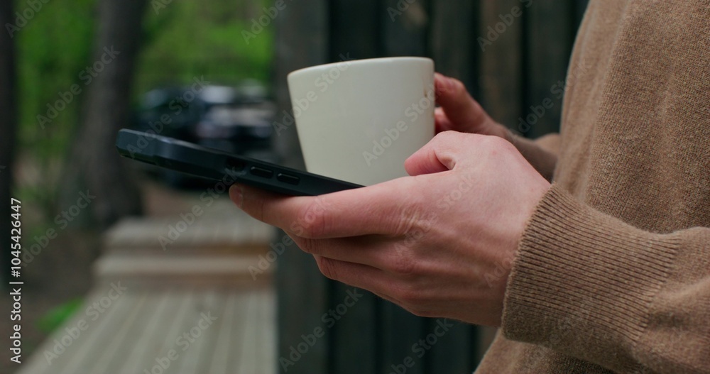 A man uses a mobile phone and drinks coffee standing on the terrace. Close-up of his hands, an unrecognizable person A man uses a mobile phone and drinks coffee standing on the terrace. Close-up of his hands, an unrecognizable person