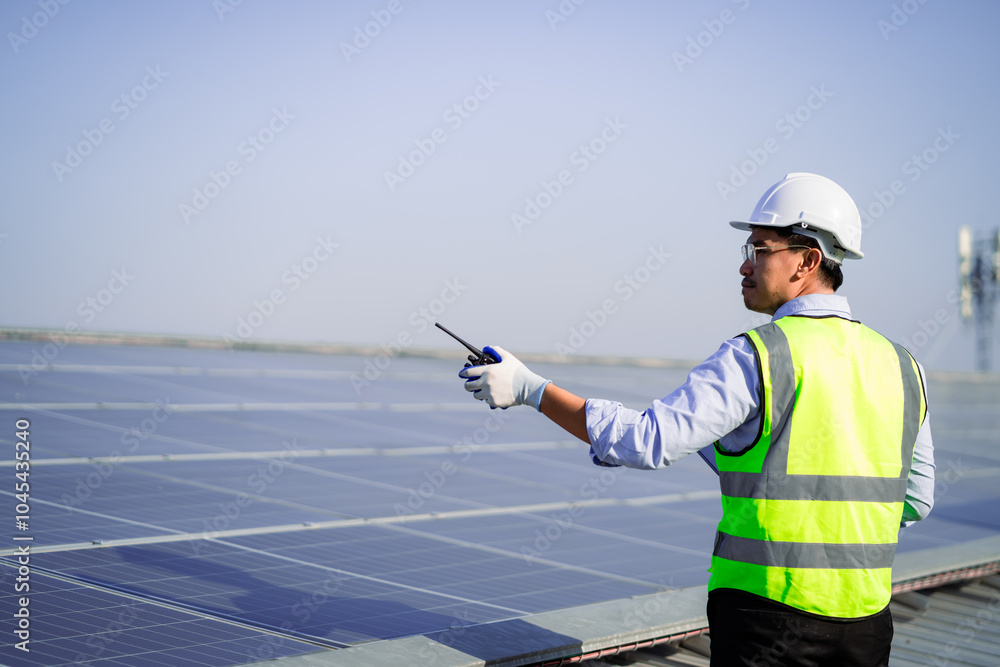 A man in a yellow vest is standing on a solar panel. He is holding a remote control and he is directing something A man in a yellow vest is standing on a solar panel. He is holding a remote control and he is directing something