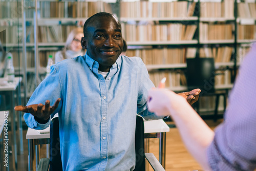Tablou pe pânză Black man shrugging shoulders while talking to tutor in library