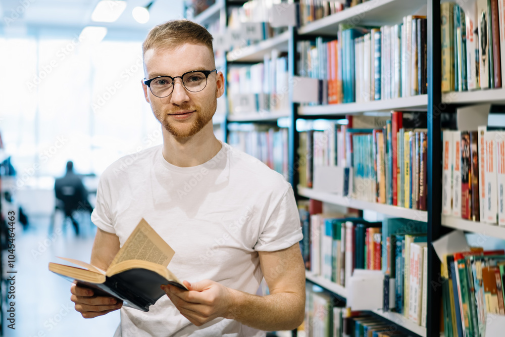 Adult guy holding opened book and looking at camera in library Adult guy holding opened book and looking at camera in library