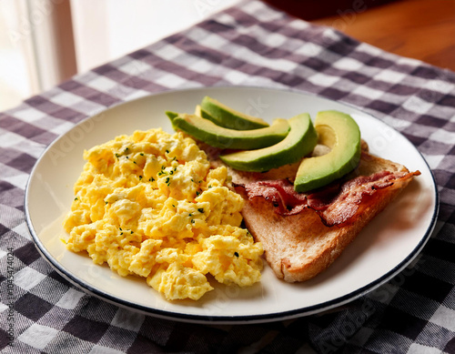 A simple breakfast featuring scrambled eggs served on a white plate. The eggs are soft and fluffy with a golden hue photo