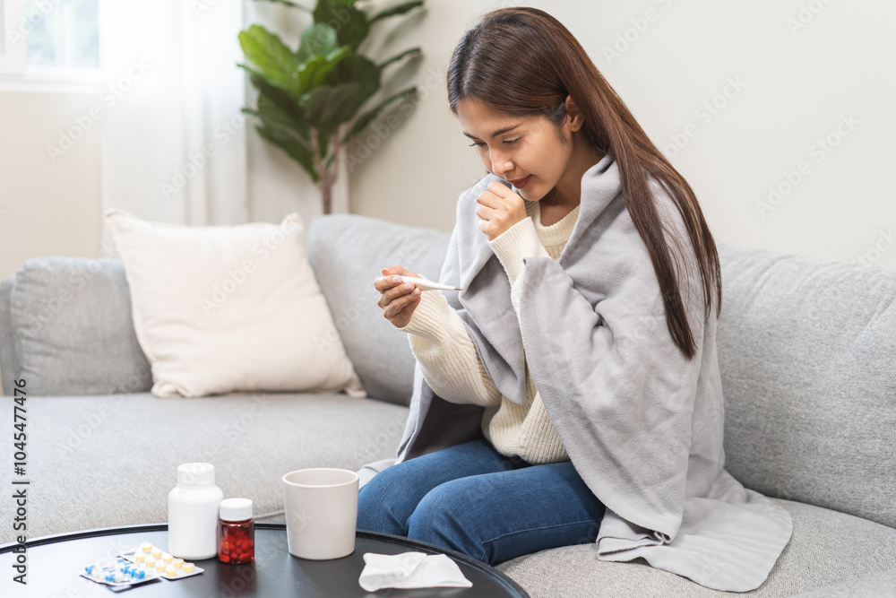 Sick, influenza asian young woman, girl have fever, cough and sore throat, holding thermometer for check measure body temperature, illness while sitting under blanket rest on sofa at home. Health care Sick, influenza asian young woman, girl have fever, cough and sore throat, holding thermometer for check measure body temperature, illness while sitting under blanket rest on sofa at home. Health care