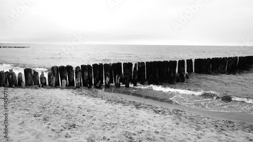 Grayscale footage of the Baltic Sea waves hitting on the wooden sticks on the beach of Dabki, Poland photo