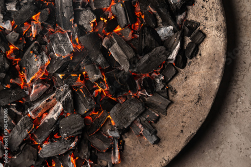 Hot coals with vibrant red and orange hues, emitting intense heat. Glowing pieces surrounded by dark ash, creating a rustic atmosphere photo