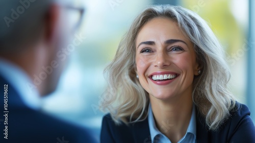 Smiling woman engages in conversation with a colleague during a meeting in a bright, modern office setting.