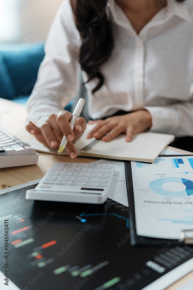 Businesswoman is analyzing financial data using a calculator and taking notes in her notebook Businesswoman is analyzing financial data using a calculator and taking notes in her notebook