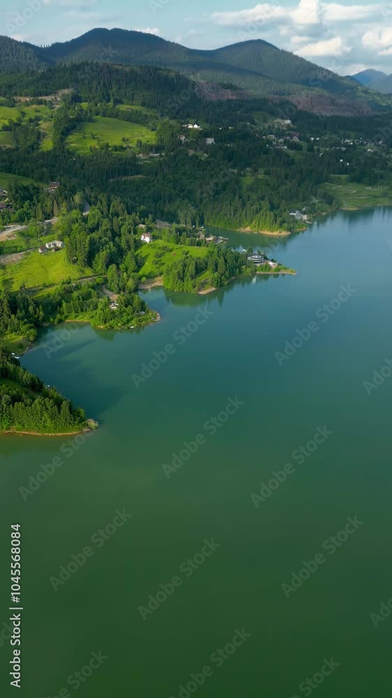 Beautiful vertical aerial perspective of Colibita Lake, Bistriţa-Năsăud, Romania. Green landscape on the Călimani mountains. Forest. Drone going forward, descending. Travel destination. Beautiful vertical aerial perspective of Colibita Lake, Bistriţa-Năsăud, Romania. Green landscape on the Călimani mountains. Forest. Drone going forward, descending. Travel destination.
