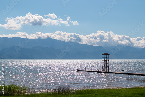 Viewing tower at the end of wooden pier on calm waters of Skadar lake near Shkoder town in Albania. Scenic view of Dinarc Alps mountains, Southern Montenegro. Shimmering water surface. Summer vacation photo