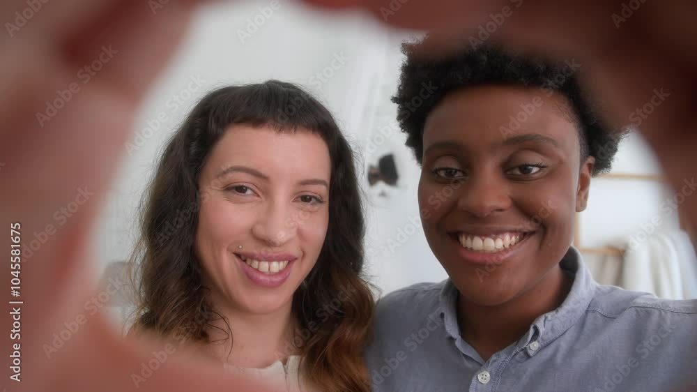 Close up portrait of lesbian couple making heart shape with hands in bedroom home Close up portrait of lesbian couple making heart shape with hands in bedroom home