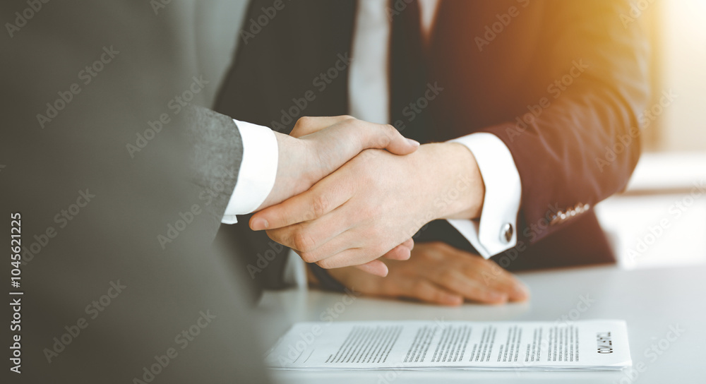 Unknown businessman shaking hands with his colleague or partner above the desk in sunny office, close-up Unknown businessman shaking hands with his colleague or partner above the desk in sunny office, close-up
