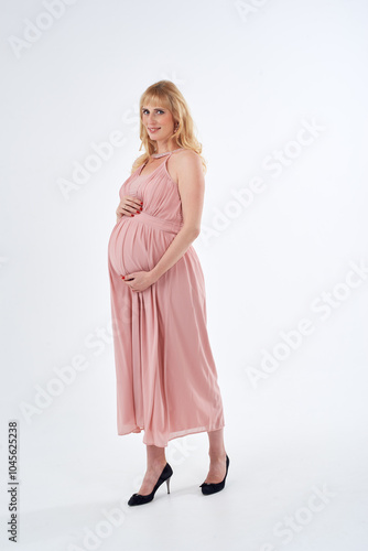 Woman in pink dress posing for photo. She is pregnant and wearing necklace. Mother love concept.
