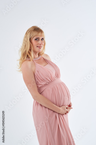 Woman in pink dress posing for photo. She is pregnant and wearing necklace. Mother love concept.