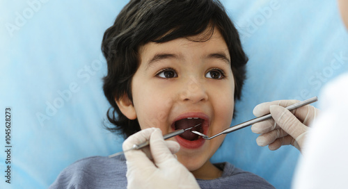 Cute arab boy sitting at dental chair with open mouth during oral checking up with doctor. Visiting dentist office. Stomatology concept