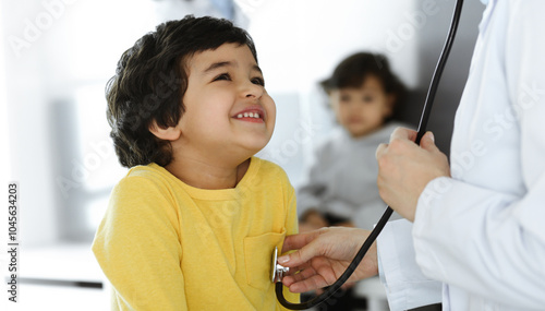 Woman-doctor examining a child patient by stethoscope. Cute arab boy at physician appointment. Medicine help concept