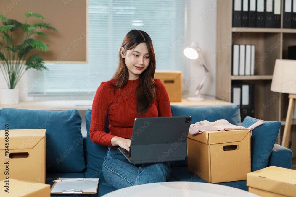Young entrepreneur managing her business from home, surrounded by cardboard boxes and using laptop Young entrepreneur managing her business from home, surrounded by cardboard boxes and using laptop